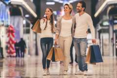Parents and their daughter are holding shopping bags.